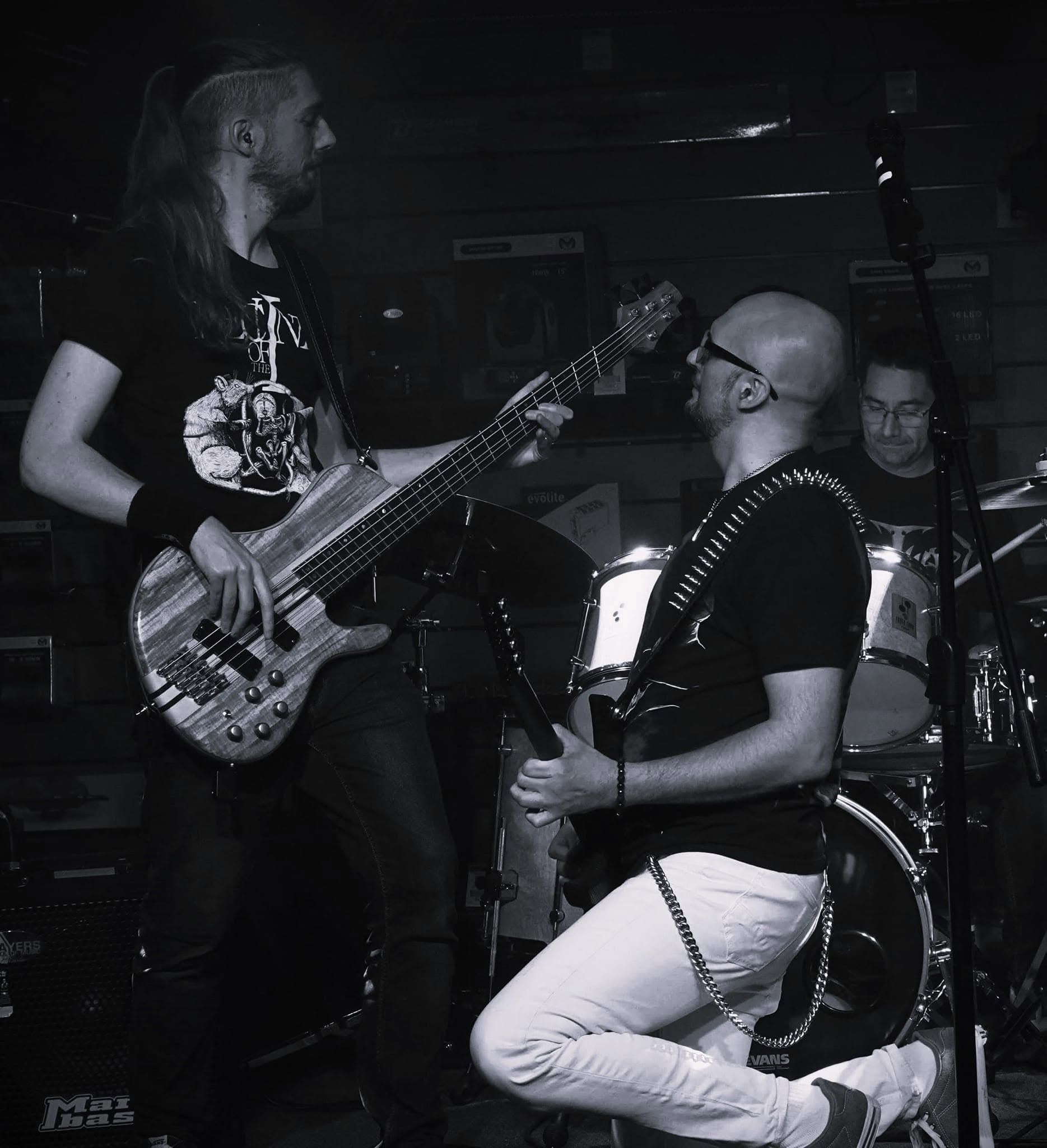 Le guitariste de 83FM à genoux devant la batterie, en noir et blanc